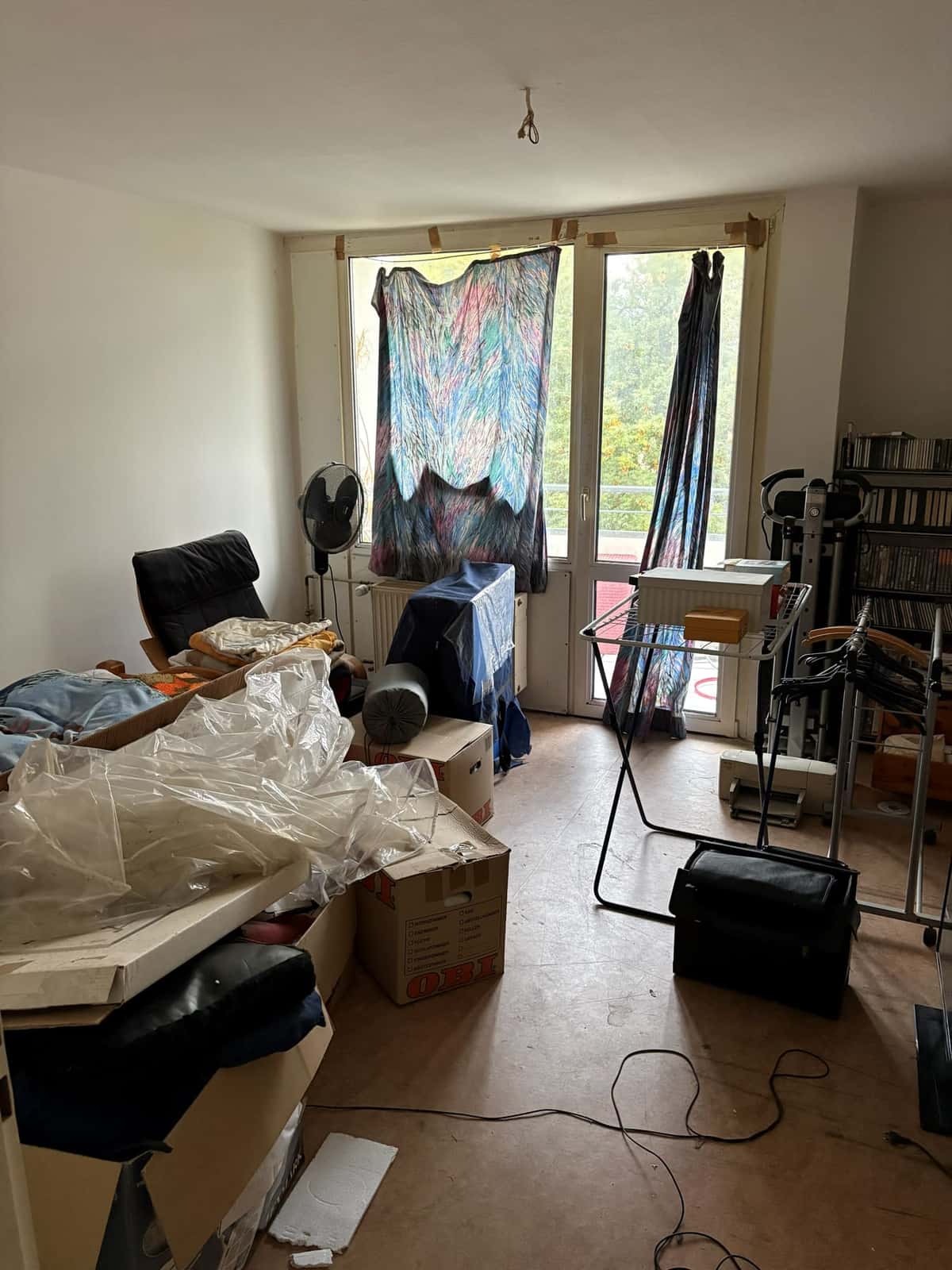 Zimmer mit Balkontür vor der Wohnungsauflösung, vollgestellt mit Möbeln, Kartons und Kleiderständer