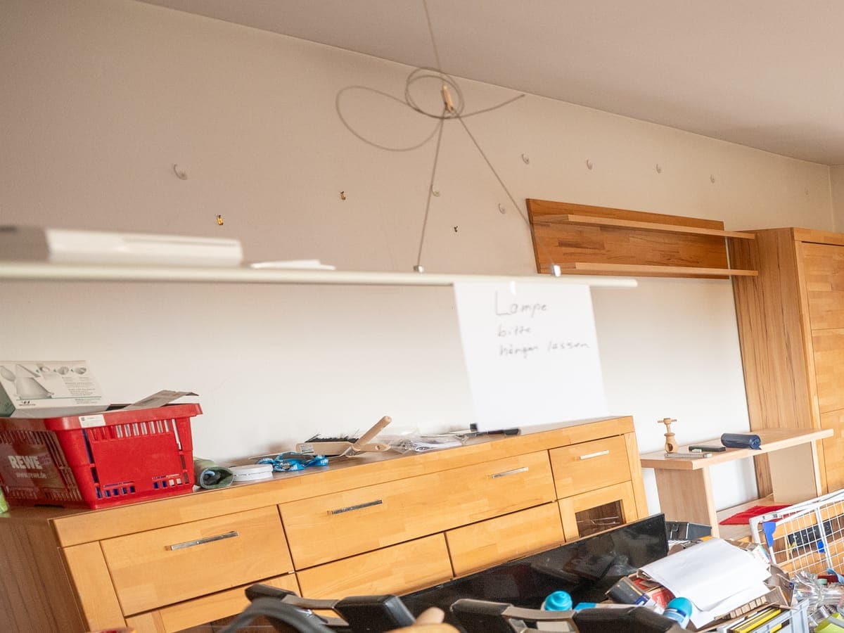 Vorher: Pendelleuchte über dem vollgestellten Sideboard mit dem handgeschriebenen Zettel „Lampe bitte hängen lassen“
